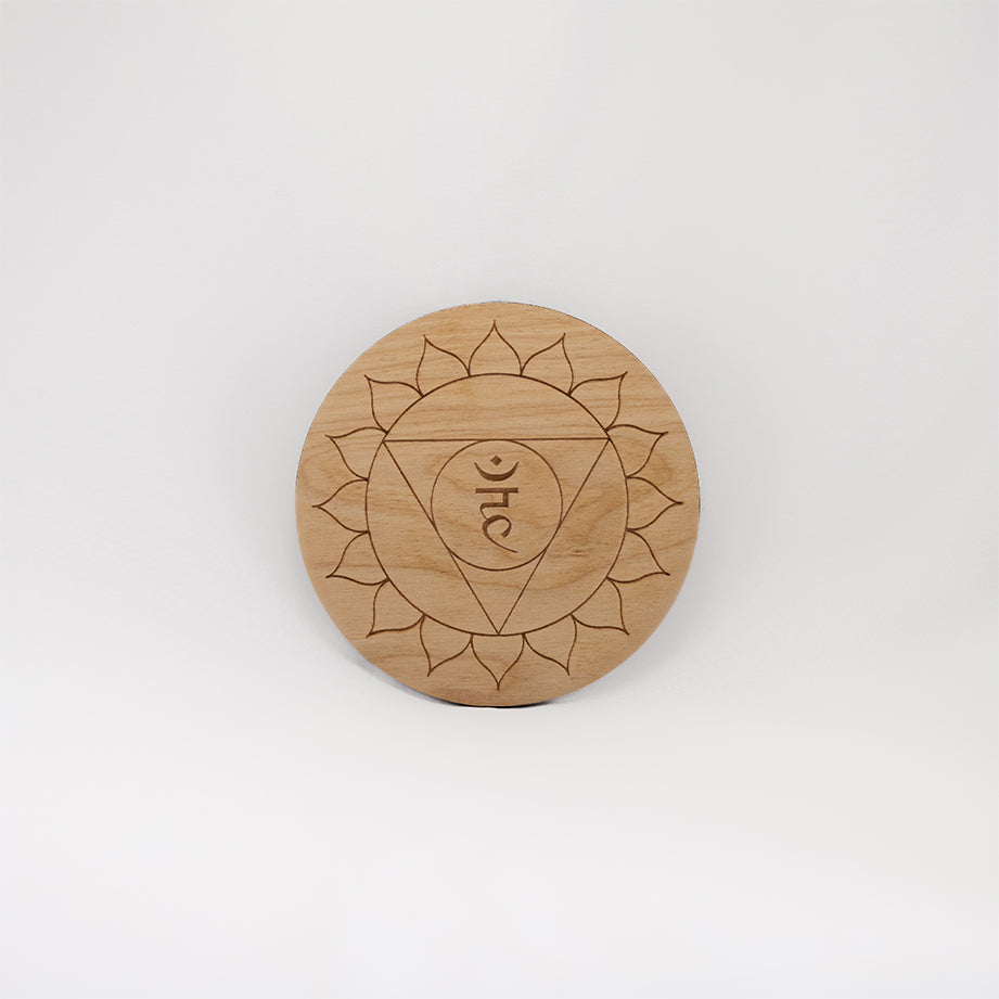 A circular wooden laser-cut crystal grid engraved with the throat chakra symbol with a plain white background. 