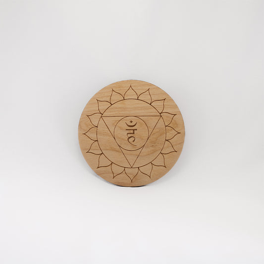 A circular wooden laser-cut crystal grid engraved with the throat chakra symbol with a plain white background. 