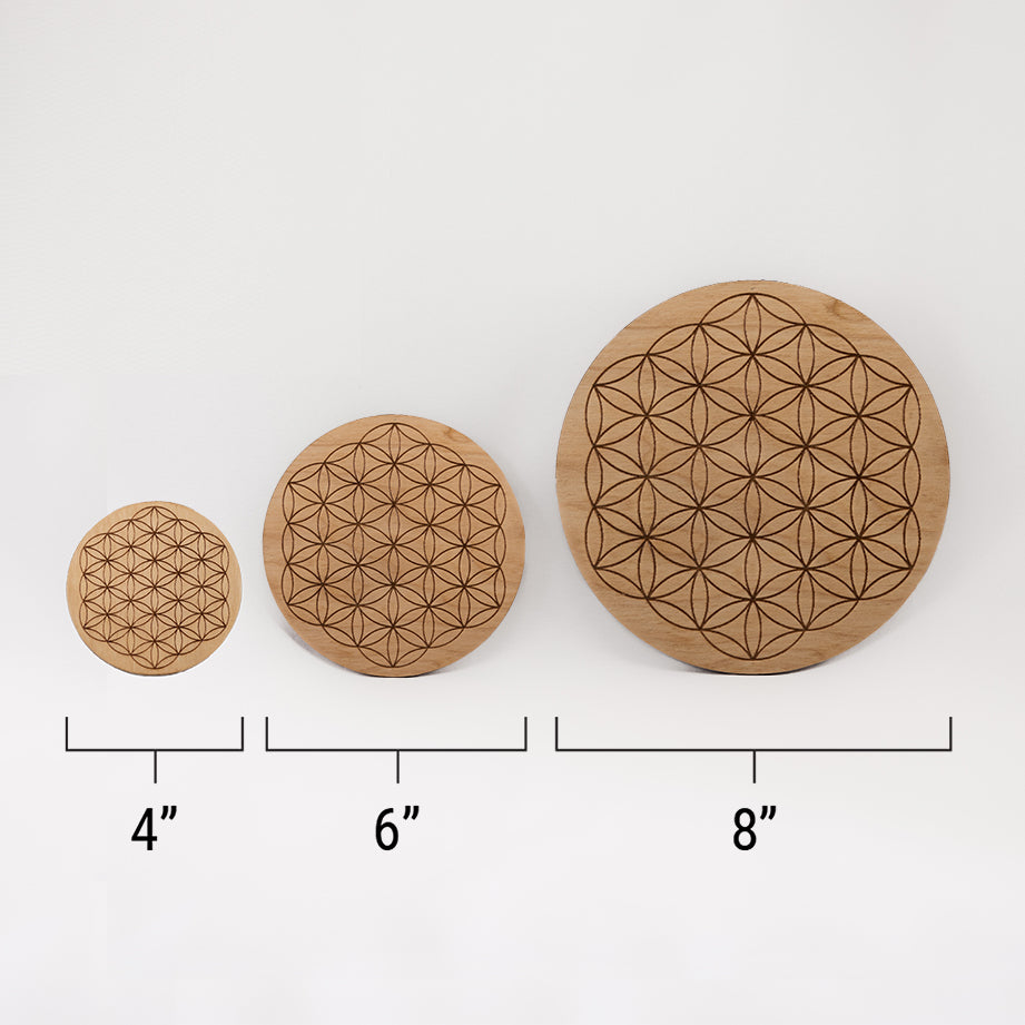 Three different sizes of the circular wooden laser-cut crystal grid engraved with the Flower of Life. against a white background with a ruler underneath all three. The smallest measuring 4", the middle 6", and the largest 8".