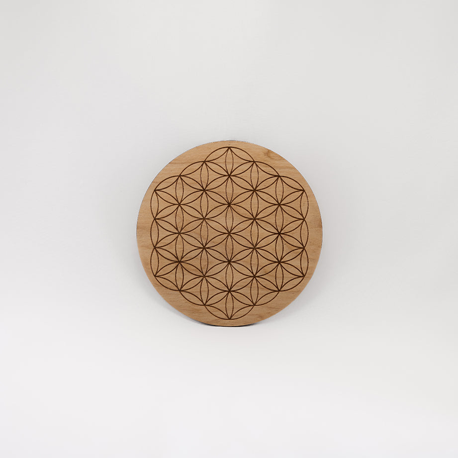 A circular wooden laser-cut crystal grid engraved with the Flower of Life with a plain white background. 