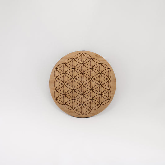 A circular wooden laser-cut crystal grid engraved with the Flower of Life with a plain white background. 