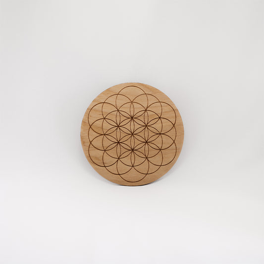 A circular wooden laser-cut crystal grid engraved with the Flower of Life with a plain white background. 