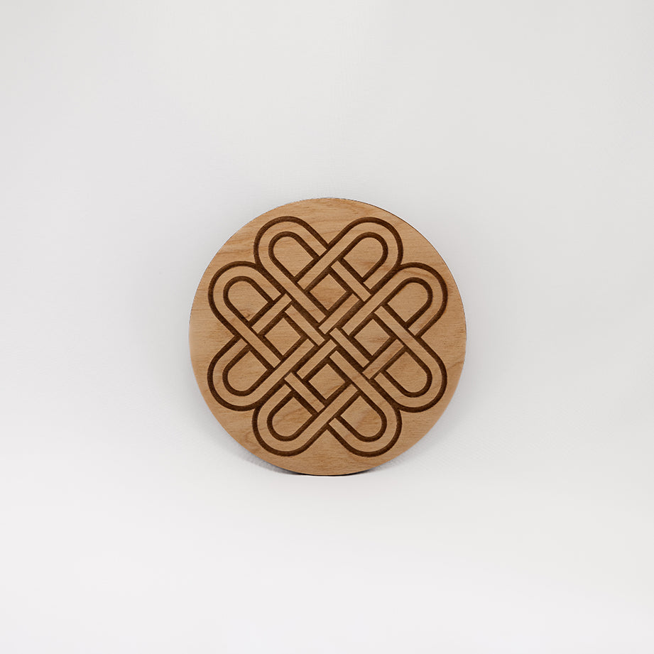 A circular wooden laser-cut crystal grid engraved with a Celtic knot with a plain white background. 