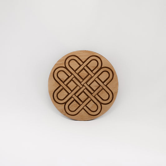 A circular wooden laser-cut crystal grid engraved with a Celtic knot with a plain white background. 