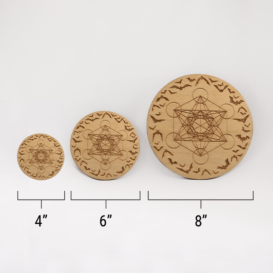 Three different sizes of the circular wooden laser-cut crystal grid engraved with Metatron's Cube and a border of bats in flight against a white background with a ruler underneath all three. The smallest measuring 4", the middle 6", and the largest 8". 
