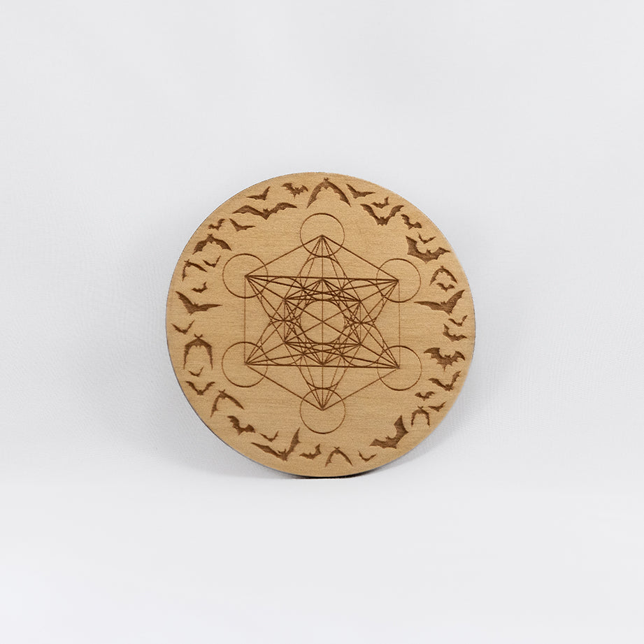 A circular wooden laser-cut crystal grid engraved with Metatron's Cube and  a border made up of bats in flight with a plain white background. 