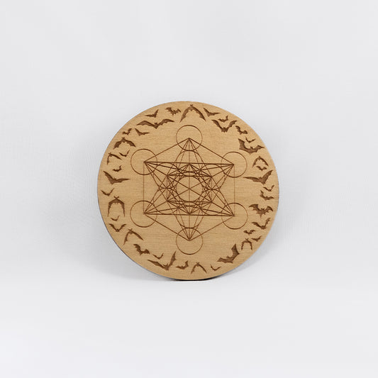 A circular wooden laser-cut crystal grid engraved with Metatron's Cube and  a border made up of bats in flight with a plain white background. 