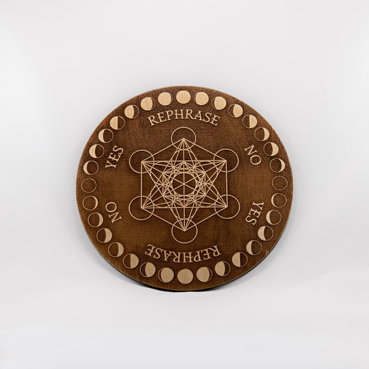 Circular baltic birch laser-cut pendulum board engraved with the words "yes", "no", "rephrase"  as well as Metatron's cube and a decorative moon phase border.