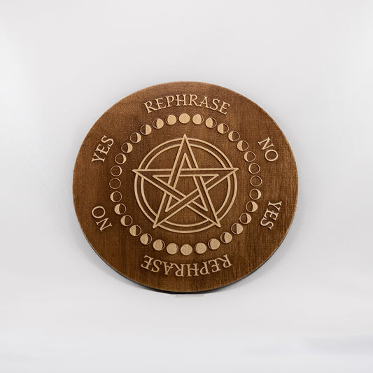 Circular Baltic birch laser-cut pendulum board engraved around its border with the words "yes", "no", "rephrase", the board has a pentacle in the centre encircled with the different moon phases.