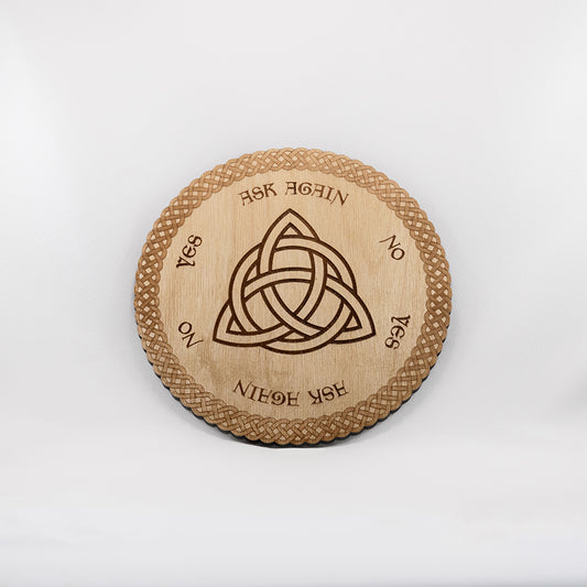 Circular Baltic birch laser-cut pendulum board engraved with the words "yes", "no", and "ask again". The centre of the board is engraved with the Celtic Triquetra symbol and the edge of the board has a die-cut braided border.