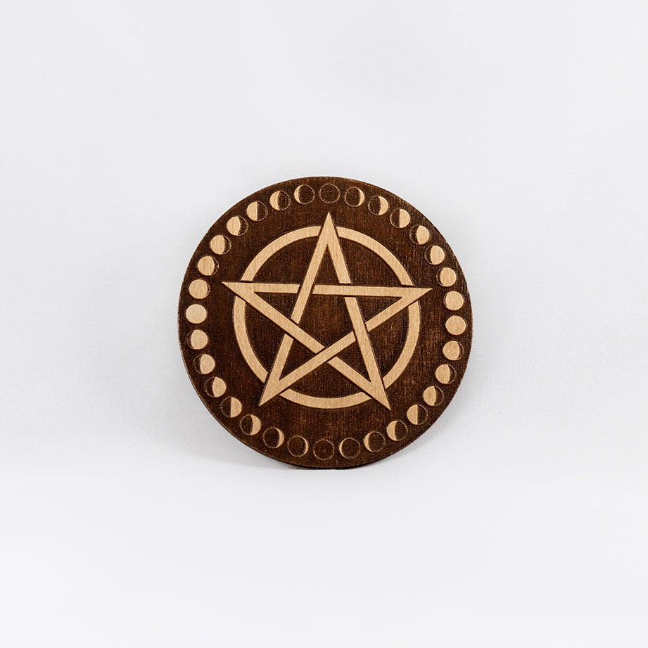 A circular wooden laser-cut crystal grid engraved with a pentacle and a border made up of the cycles of the moon with a plain white background. 