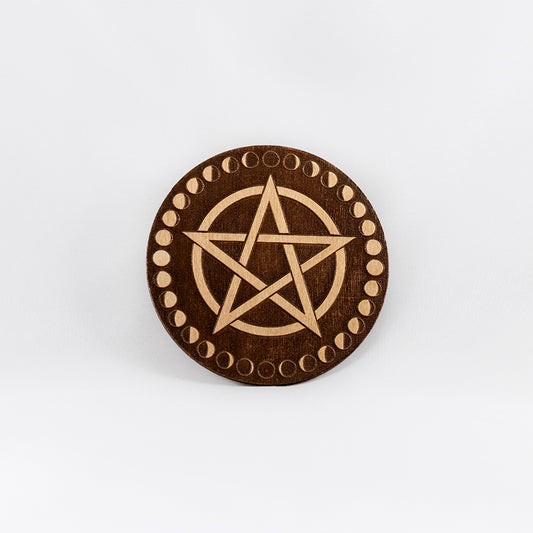 A circular wooden laser-cut crystal grid engraved with a pentacle and a border made up of the cycles of the moon with a plain white background. 