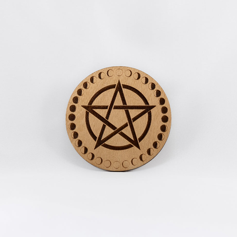 A circular wooden laser-cut crystal grid engraved with a pentacle and a border made up of the cycles of the moon with a plain white background. 