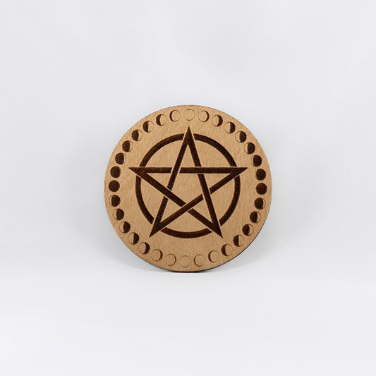 A circular wooden laser-cut crystal grid engraved with a pentacle and a border made up of the cycles of the moon with a plain white background.