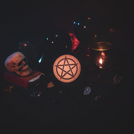 A circular wooden laser-cut crystal grid engraved with a Pentacle. The grid sits amongst candles, crystal balls, a skull, tarot cards and assorted crystals.