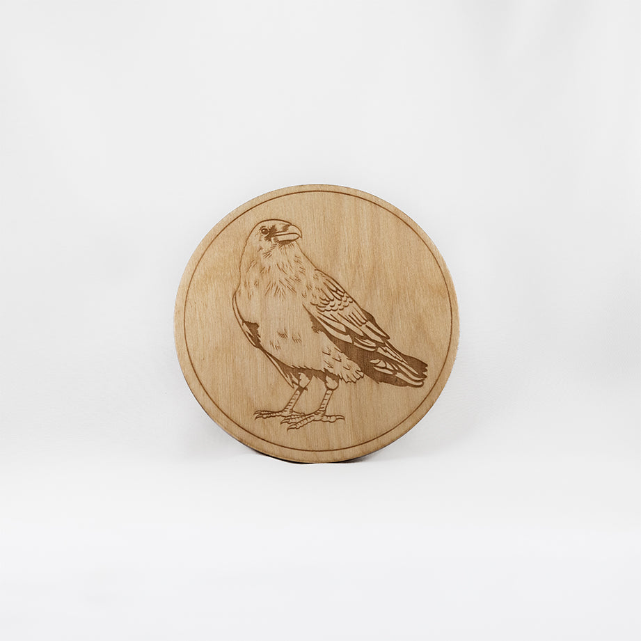 A circular wooden laser-cut crystal grid engraved with a raven with a plain white background. 