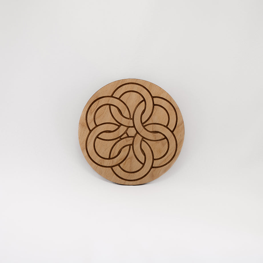 A circular wooden laser-cut crystal grid engraved with a Celtic ring knot with a plain white background. 