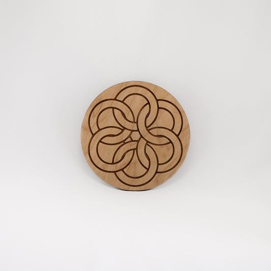 A circular wooden laser-cut crystal grid engraved with a Celtic ring knot with a plain white background.