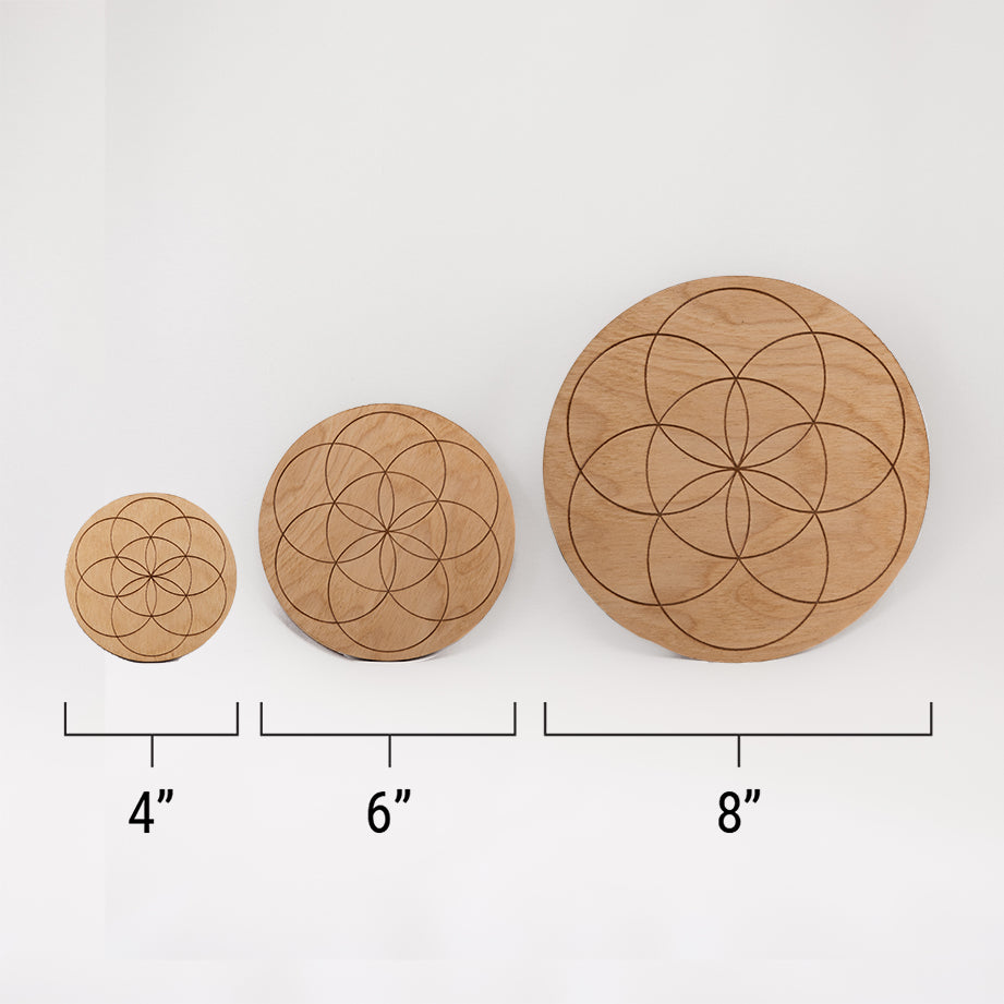 Three different sizes of the circular wooden laser-cut crystal grid engraved with the Seed of Life. against a white background with a ruler underneath all three. The smallest measuring 4", the middle 6", and the largest 8".