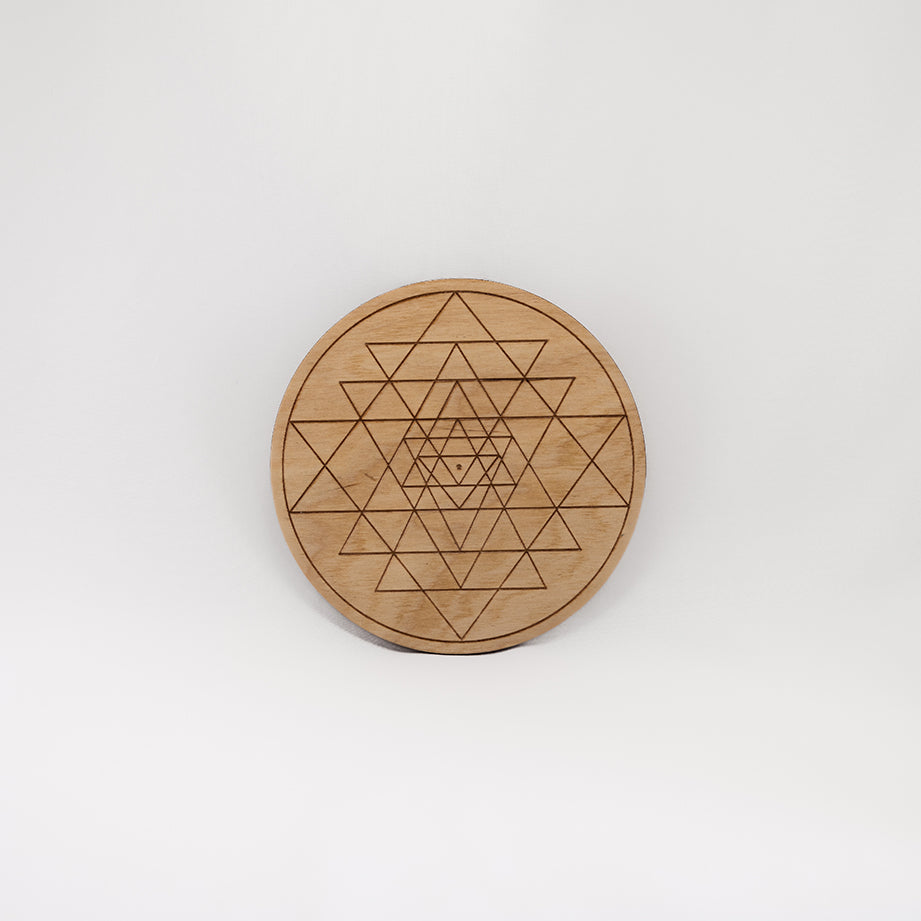 A circular wooden laser-cut crystal grid engraved with Sri Yantra with a plain white background. 