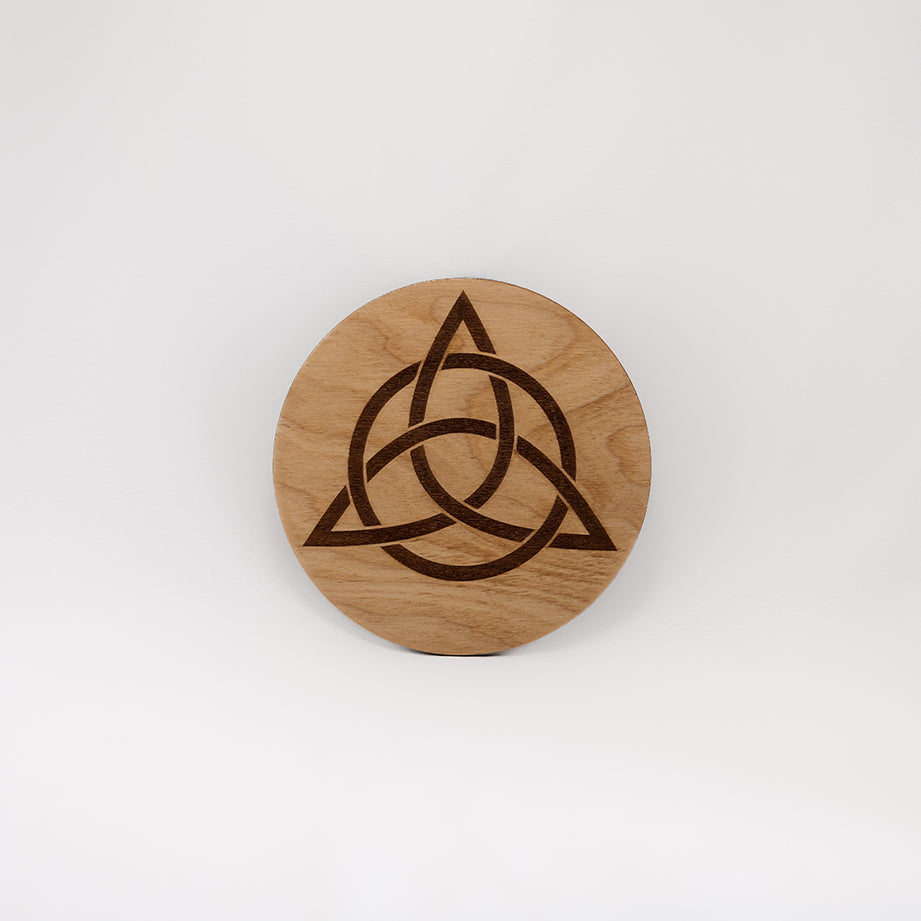 A circular wooden laser-cut crystal grid engraved with the Celtic Triquetra symbol with a plain white background. 