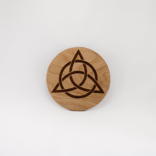 A circular wooden laser-cut crystal grid engraved with the Celtic Triquetra symbol with a plain white background. 