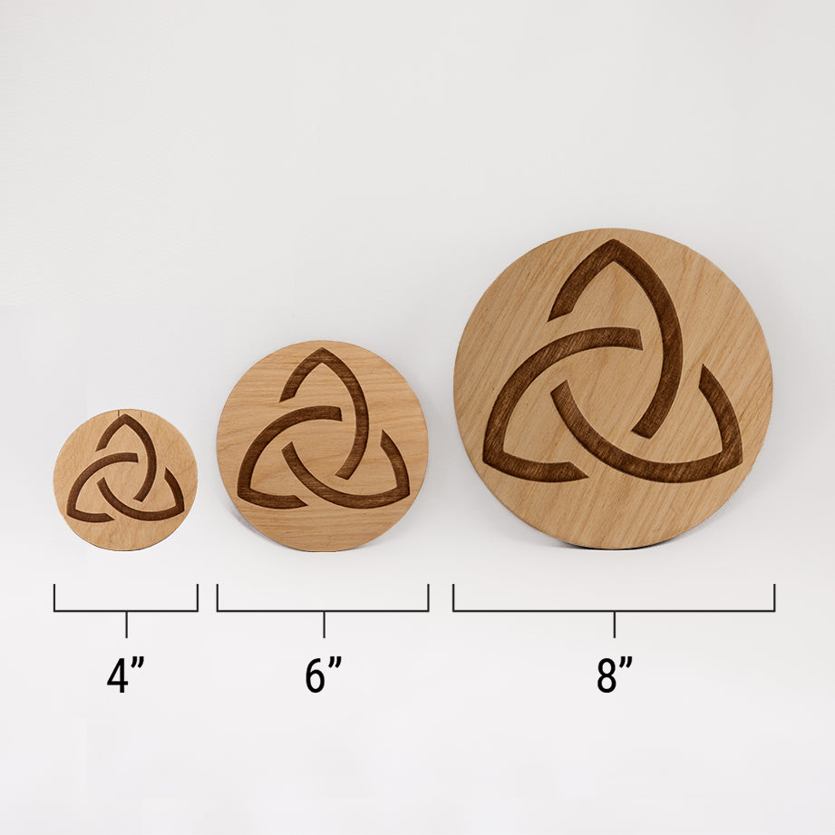 Three different sizes of the circular wooden laser-cut crystal grid engraved with the Celtic Triquetra symbol against a white background with a ruler underneath all three. The smallest measuring 4", the middle 6", and the largest 8".