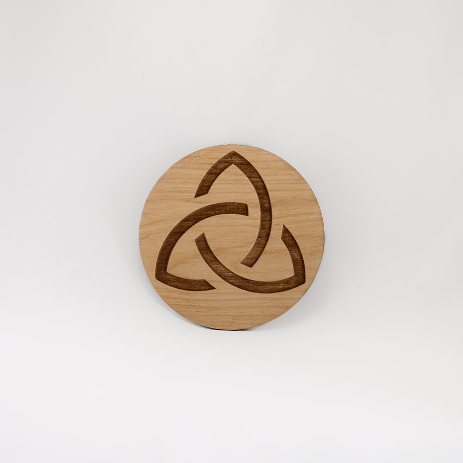 A circular wooden laser-cut crystal grid engraved with the Celtic Triquetra symbol with a plain white background. 