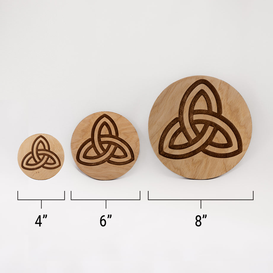 Three different sizes of the circular wooden laser-cut crystal grid engraved with the Celtic Triquetra symbol against a white background with a ruler underneath all three. The smallest measuring 4", the middle 6", and the largest 8".