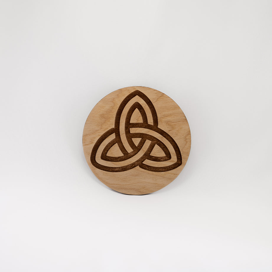 A circular wooden laser-cut crystal grid engraved with the Celtic Triquetra symbol with a plain white background. 