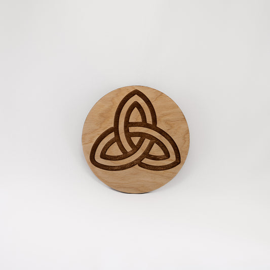 A circular wooden laser-cut crystal grid engraved with the Celtic Triquetra symbol with a plain white background.