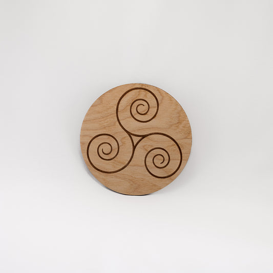 A circular wooden laser-cut crystal grid engraved with the Celtic Triskelion symbol with a plain white background.