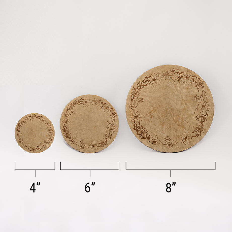 Three different sizes of the circular wooden laser-cut crystal grid engraved with a border of wildflowers against a white background with a ruler underneath all three. The smallest measuring 4", the middle 6", and the largest 8".
