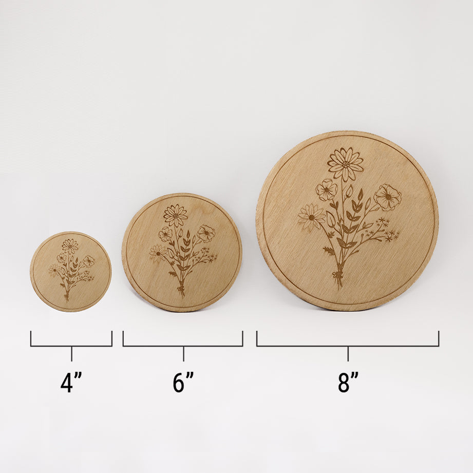 Three different sizes of the circular wooden laser-cut crystal grid engraved in the centre with a bouquet of wildflowers against a white background with a ruler underneath all three. The smallest measuring 4", the middle 6", and the largest 8".