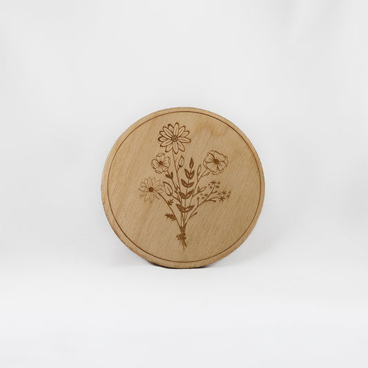 A circular wooden laser-cut crystal grid engraved in the centre with a bouquet of wildflowers with a plain white background. 